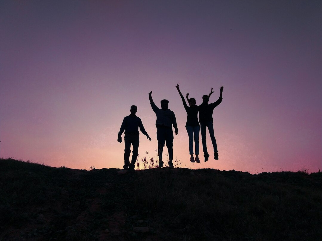 Group of cheerful young people jumping outdoors with raised arms